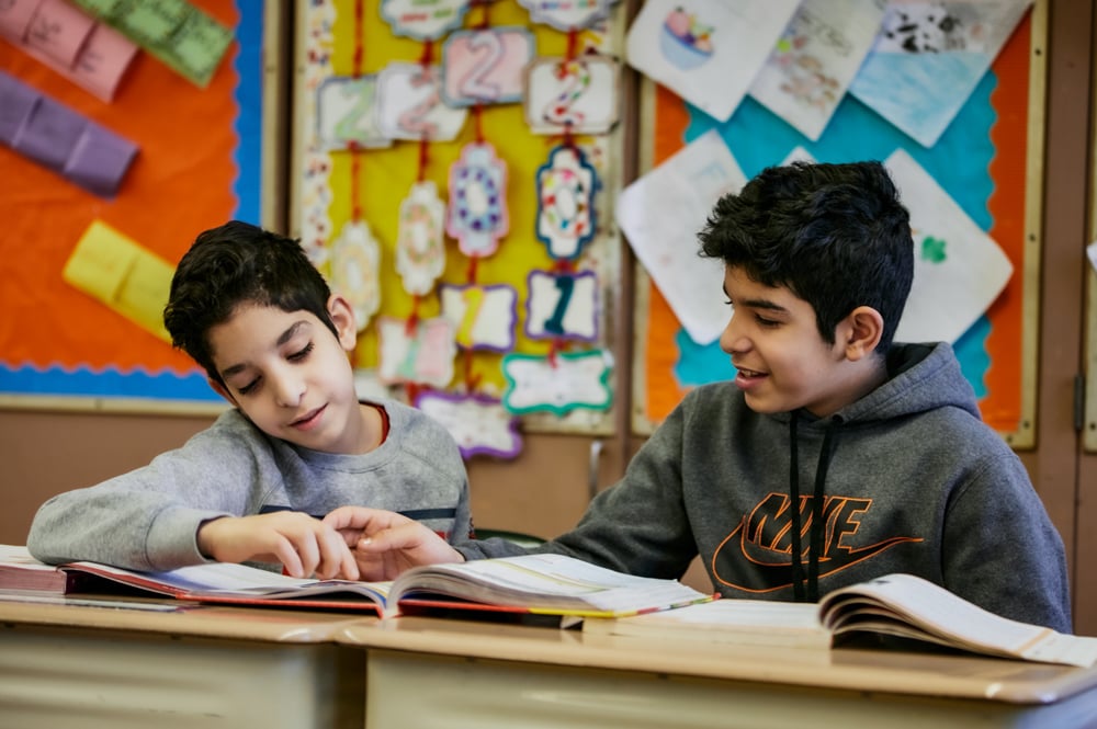 Two students study from a book at their desks.