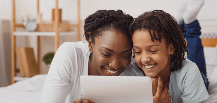 A parent and child look at a computer together and smile. 