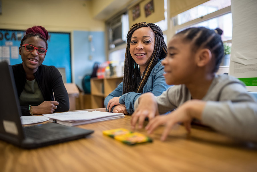 A teacher, student, and parent chat around a desk. 