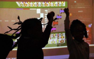 Students dancing in silhouette against a projection on a classroom wall. 