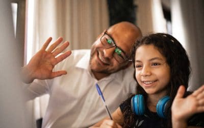 A family partner and child smile and wave towards a computer screen.